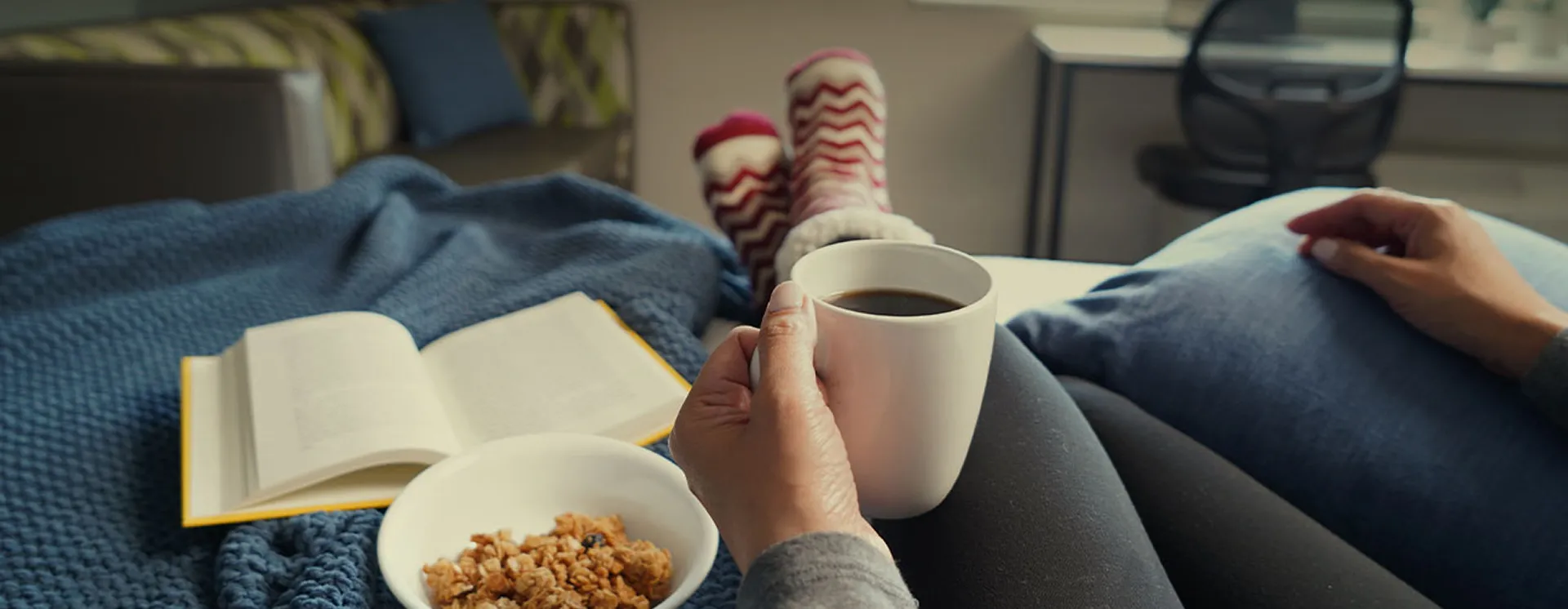 Person relaxing in bed with coffee, an open book and snacks